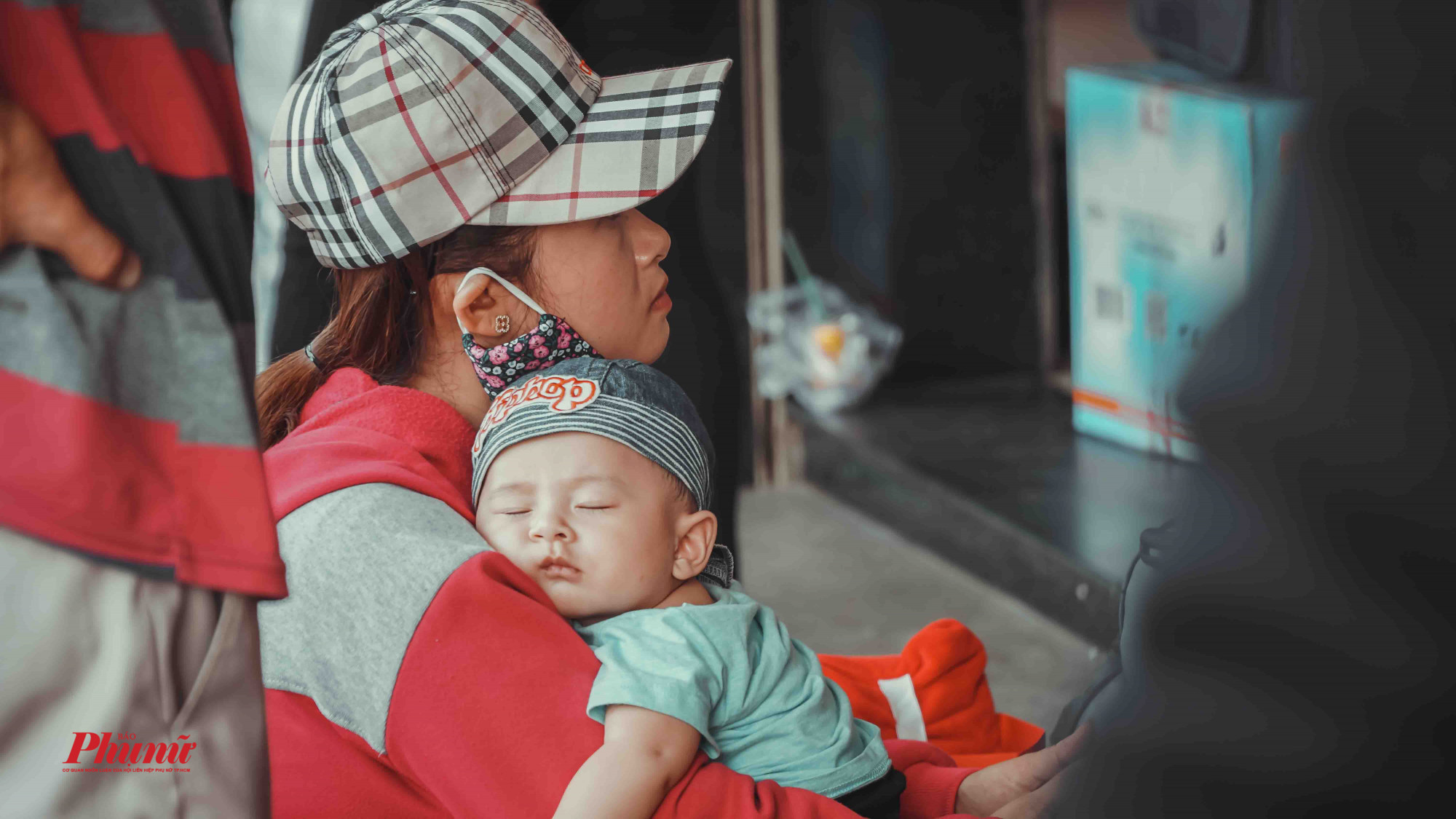 Một bé trai mệt nhừ ngủ trên vai mẹ