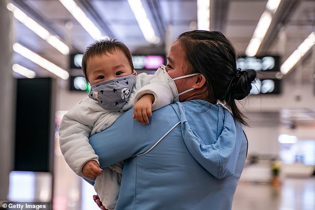 Một người phụ nữ bế em bé đeo khẩu trang khi họ ra khỏi sảnh đến tại ga đường sắt cao tốc Hồng Kông vào ngày 29/1.