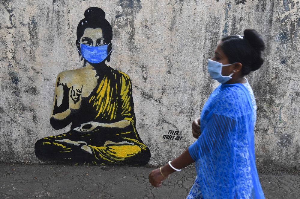 Một phụ nữ đeo khẩu trang đi ngang qua bức tranh tường vẽ Đức Phật cũng đeo khẩu trang, trong nỗi lo ngại về đại dịch COVID-19 có thể bùng phát dữ dội ở Ấn Độ. Ảnh: Indranil Mukherjee (AFP Photo). 