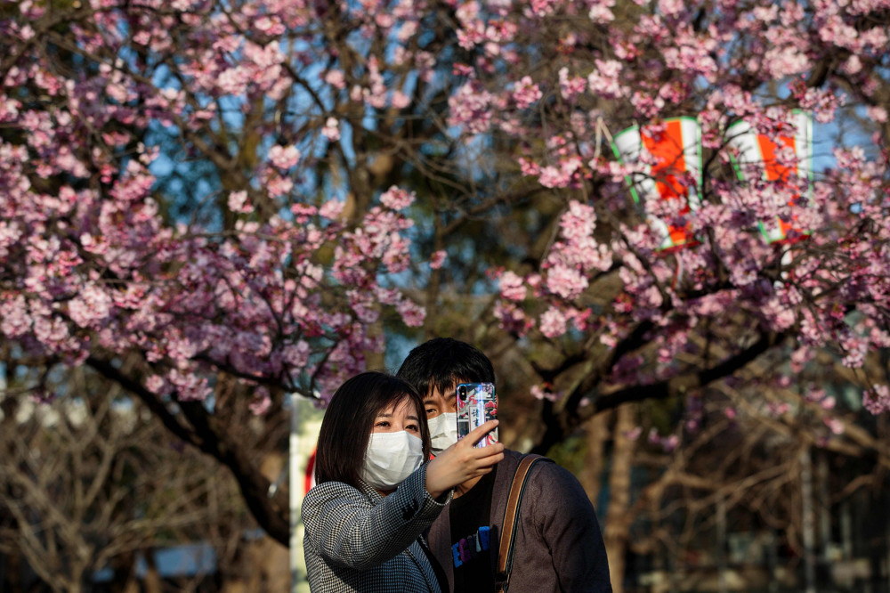 Một cặp đôi cùng chụp hình selfie với hoa anh đào tại công viên Ueno ở thủ đô Tokyo, Nhật Bản. Chính quyền Tokyo đã kêu gọi người dân hạn chế tham gia các bữa tiệc ở công viên trong mùa hoa anh đào năm nay, để tránh làm lây lan dịch COVID-19. Ảnh: Behrouz Mehri (AFP Photo).