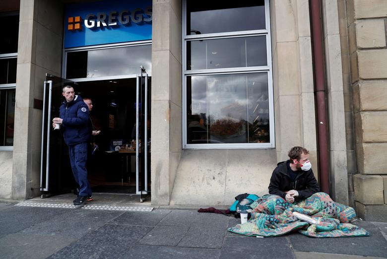 Nguòi vô gia cư quấn chăn ngồi trước một cửa hàng vẫn còn mở cửa vào ngày 17/3 tại Newcastle, Anh.