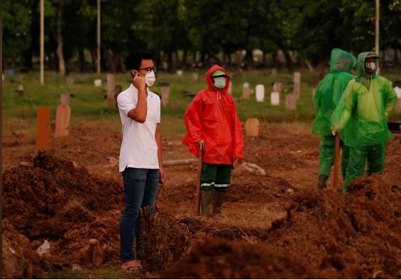 Người con trai Firos đứng nhìn quan tài người mẹ được hạ huyệt từ xa. Ảnh: Reuters