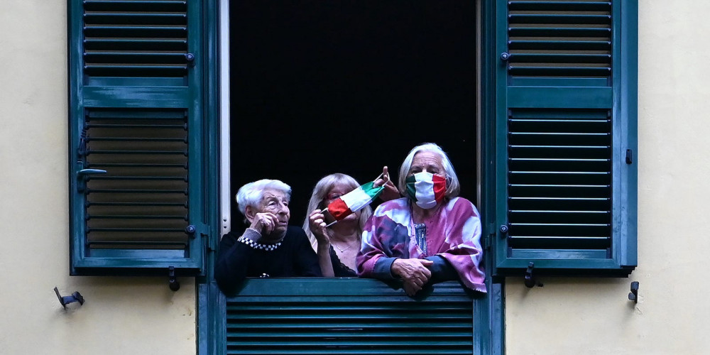 Những người có mặt nạ bảo vệ nhìn từ cửa sổ của họ vào các nghệ sĩ biểu diễn trong sân của một tòa nhà chung cư nổi tiếng cho buổi trình diễn Sotto lo Stesso Cielo (tour du lịch Under the Same Sky) ở vùng ngoại ô San Basilio của Rome vào ngày 18 tháng 4 năm 2020