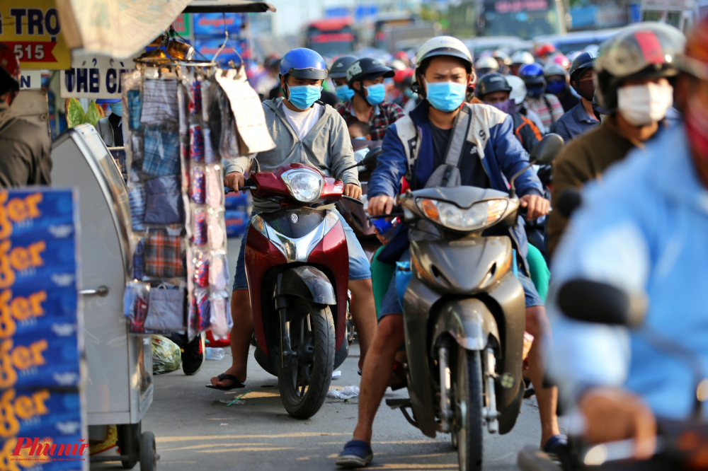 Xe máy ô tô xếp hàng dài trên quốc lộ 1A đoạn giao lộ Nguyễn Hữu Trí đến cầu vượt Bình Điền, huyện Bình Chánh, Do lượng xe cộ quá đông, nhiều người đi xe máy leo lên cả vỉa hè dành cho người đi bộ để vượt qua đoạn đường ùn ứ
