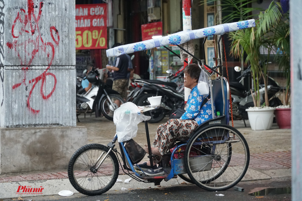 Cô bán vé số ngồi nhìn mưa khi những tờ vé số đã được che chắn cẩn thận