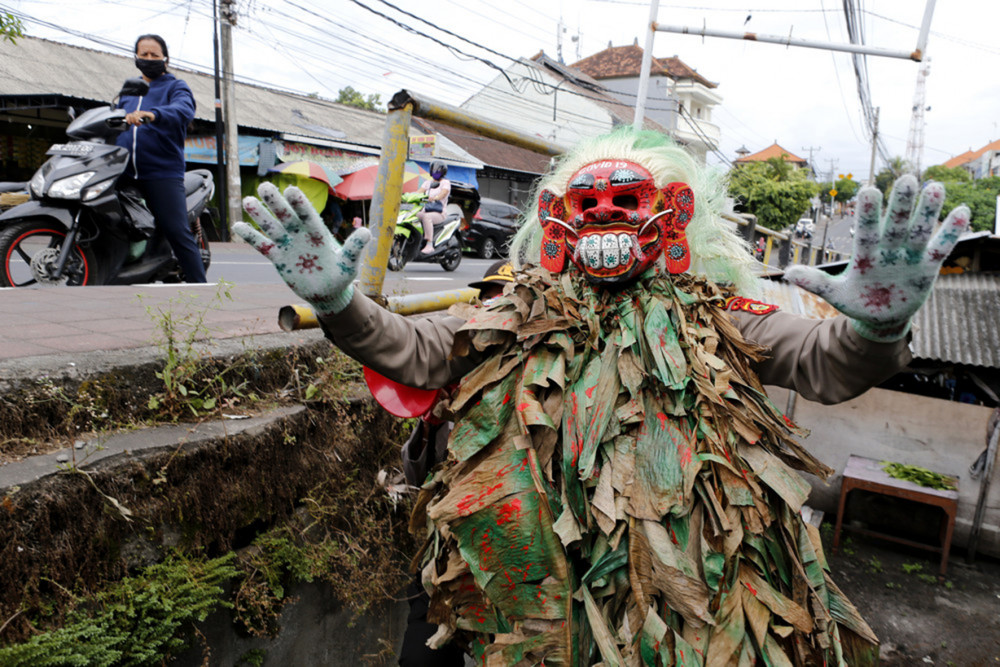 Một viên cảnh sát đeo mặt nạ truyền thống Celuluk của đảo Bali khi tuần tra tại một khu chợ ở Bali, hôm 14/5/2020. Indonesia đã triển khai 340.000 cảnh sát và binh sĩ ở 20 thành phố để đảm bảo người dân tuân thủ các quy định về đeo khẩu trang ở nơi công cộng, và giữ khoảng cách an toàn để ngăn sự lây nhiễm virus (AP Photo).