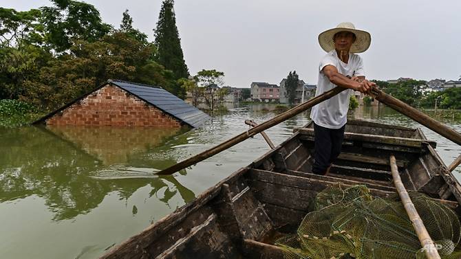 Người đàn ông chèo thuyền đi qua mái nhà bị ngập tại khu vực hồ Bà Dương