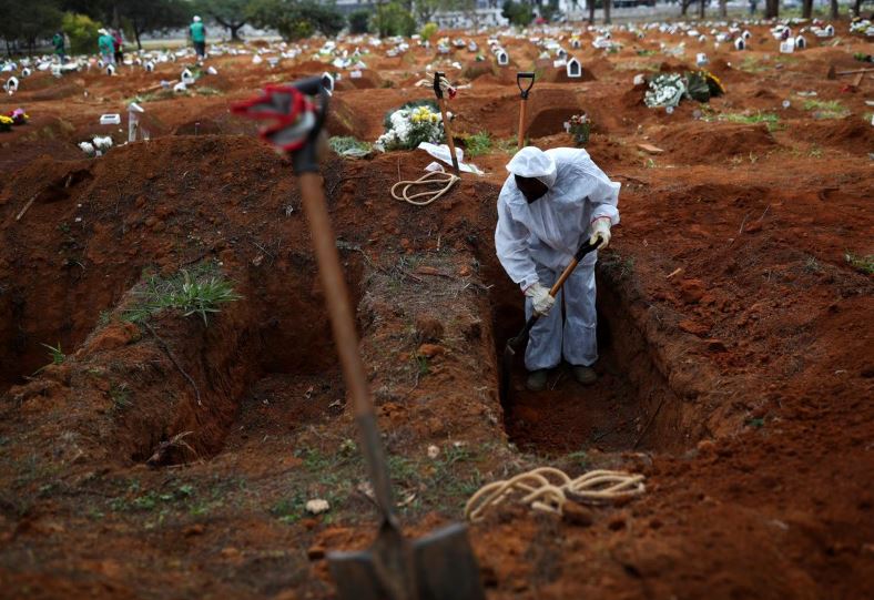 Người đào mộ mặc bộ đồ bảo hộ đã đào một ngôi mộ để chôn cất quan tài của một bệnh nhân COVID-19, tại nghĩa trang Vila Formosa, Sao Paulo, Brazil.