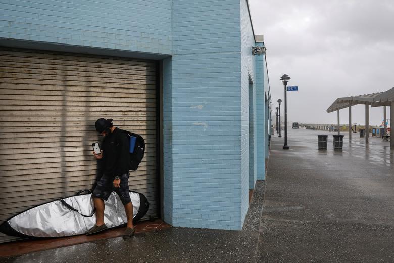 Một người lướt ván nấp bên cạnh một toà nhà để tránh những cơn gió mạnh quật vào người tại bờ biển ở New York.