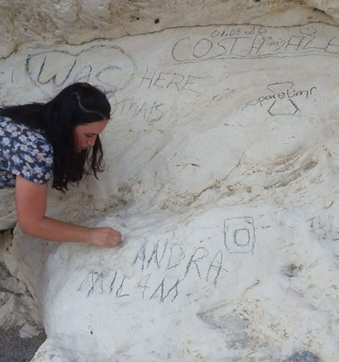 Một tình nguyện viên đang khắc phục hành vi vẽ bậy của ngôi sao Milam trên vách đá 180 năm tuổi.