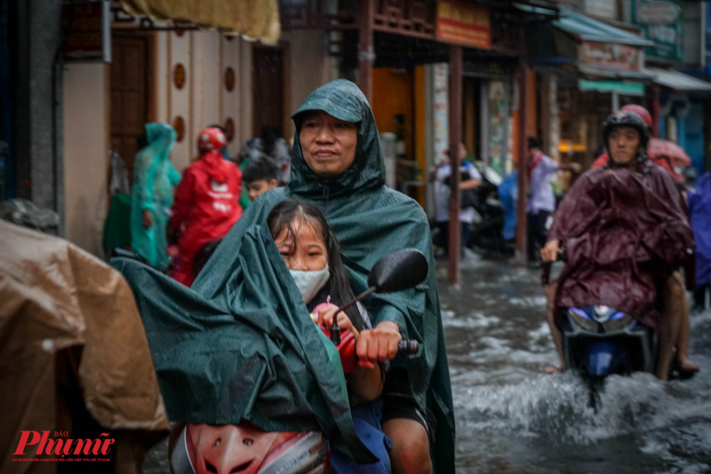 Mọt em học sinh núp trong áo mưa của phụ huynh vì trời vãn đang mưa nặng hạt