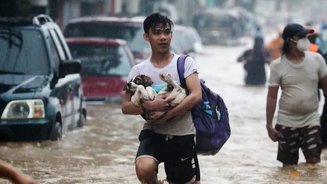 Người dân mang theo đồ đạc băng qua một con phố ngập lụt để đến nơi trú ẩn ở thành phố Marikini, ngoại ô Manila, hôm 12/11 - Ảnh: AFP