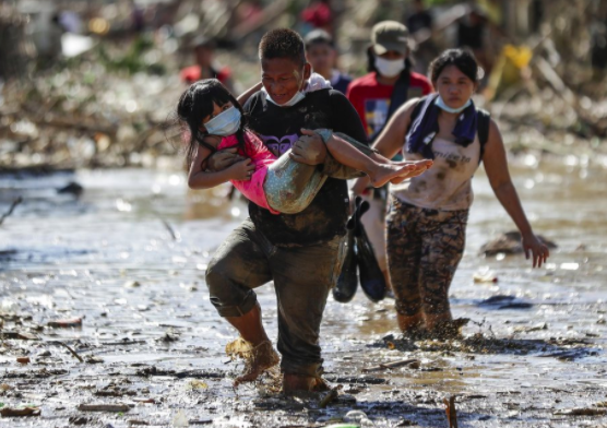 Một cảnh sát mang đồ đạc của mình băng qua các mảnh vỡ và bùn tại ngôi làng Kasiglahan bị thiệt hại do bão ở Rodriguez, tỉnh Rizal, Philippines vào thứ Sáu, ngày 13 tháng 11 năm 2020. Bùn dày và mảnh vỡ bao phủ nhiều ngôi làng xung quanh thủ đô Philippines hôm thứ Sáu sau khi bão Vamco gây ra lũ lụt trên diện rộng khiến cư dân phải chạy trốn lên mái nhà của họ và giết chết hàng chục người. (Ảnh AP / Aaron Favila)