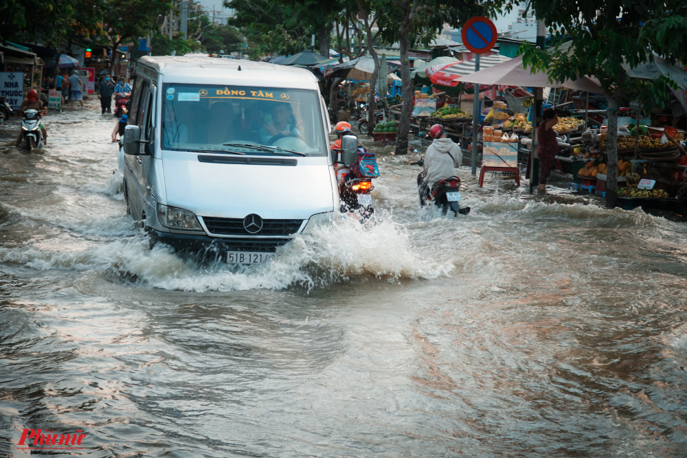 Một chiếc xe lớn chạy qua, nước tạo thành làn sống mạnh, ập vào các phương tiện xe máy, khiến nhiều người loạn choang té ngã