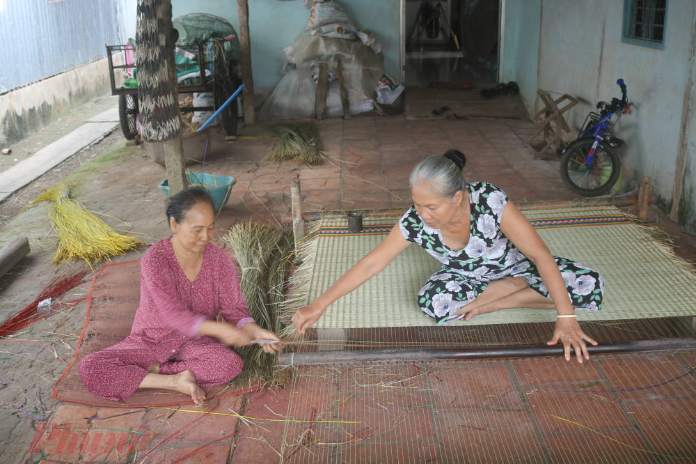 Bà Sáu Lệ (71 tuổi, áo đỏ) cùng em gái là cô Ba Kim đang dệt chiếu bằng khung dệt truyền thống