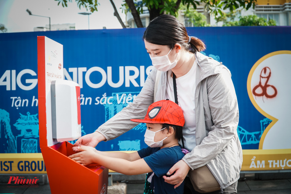 Một phụ huynh hướng dẫn con rửa tay ở đường hoa Nguyễn Huệ - Ảnh: Tam Nguyên