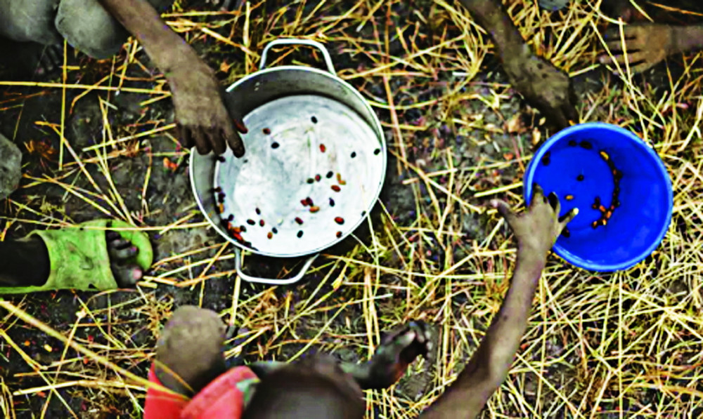 Trẻ em nhặt ngũ cốc rơi vãi trên đồng từ những chiếc túi cứu trợ ở Nam Sudan - Ảnh: AFP