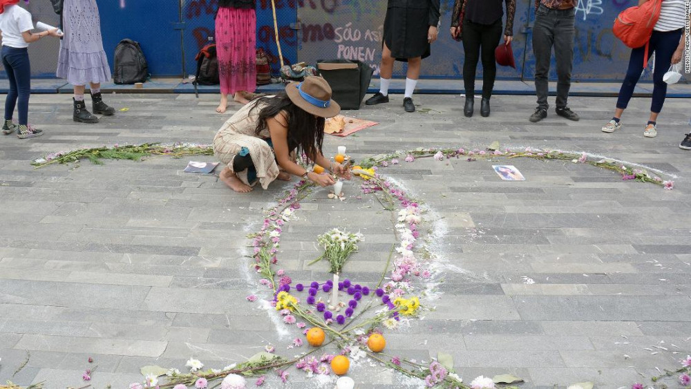 Một người phụ nữ đặt nến lên một bia mộ giả, tượng trưng cho các nạn nhân bị giết hại phụ nữ trong cuộc biểu tình Ngày Quốc tế Phụ nữ vào ngày 8 tháng 3 năm 2021 tại Thành phố Mexico