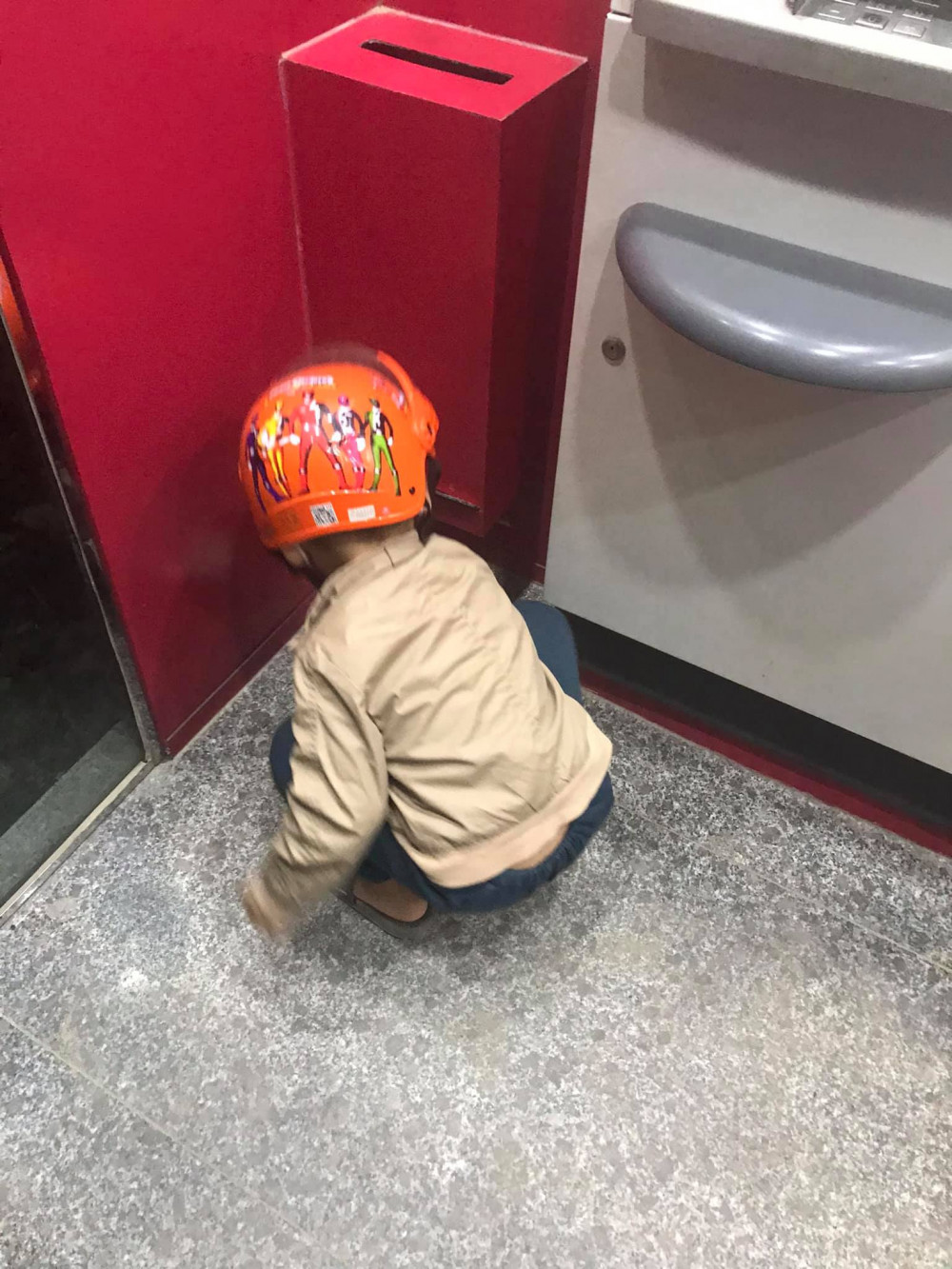 Cậu bé loay hoay nhặt những tờ biên lai dưới sàn ở một máy ATM. Ảnh từ Facebook