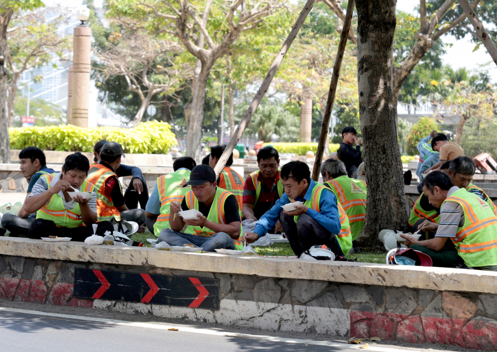 Công nhân tại vòng xoay Công Trường Mê Linh (quận 1) tranh thủ bóng cây gần đó để ăn trưa và nghỉ ngơi trước khi vào giờ làm việc chiều.