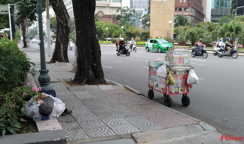 Người bán dạo đậu xe kem của mình ở ven đường Tôn Đức Thắng (Q1), ngả đầu lên chai nước suối dưới bóng mát để ngủ trưa. Anh đã bán hàng rong được 3 - 4 năm nay. Khi được hỏi thường nghỉ trưa chỗ nào, người đàn ông trả lời: 'Chỗ nào mát thì ghé vào nằm chỗ đó thôi.'