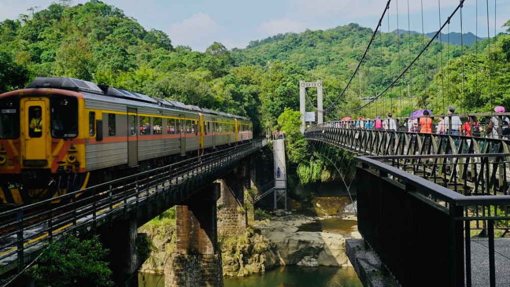 Ảnh chụp năm 2018 cho thấy khách du lịch đi bộ trên một cây cầu treo ở khu vực thác nước Shihfen trong khi tàu hỏa băng qua đường hầm trên tuyến đường song song, ở thành phố Tân Đài Bắc.