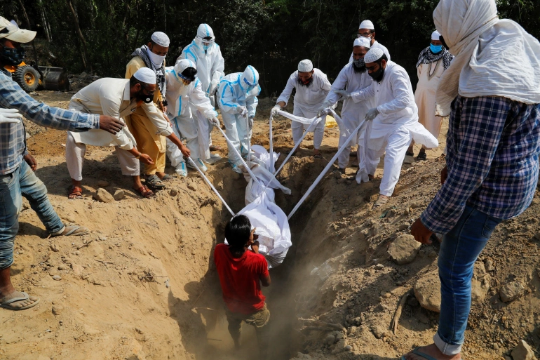 Nhân viên nghĩa trang hạ xác một người đàn ông chết vì COVID-19 xuống mộ ở New Delhi