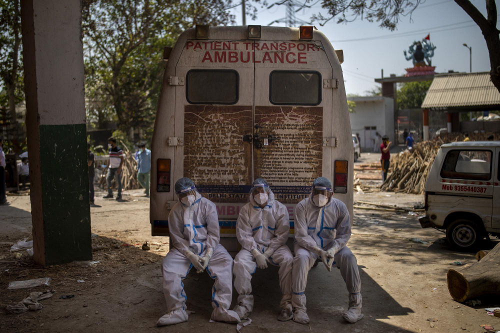 Những công nhân mệt mỏi, chịu trách nhiệm mang xác chết đi hỏa táng, ngồi trên bậc sau của xe cấp cứu bên trong một lò hỏa táng, ở New Delhi