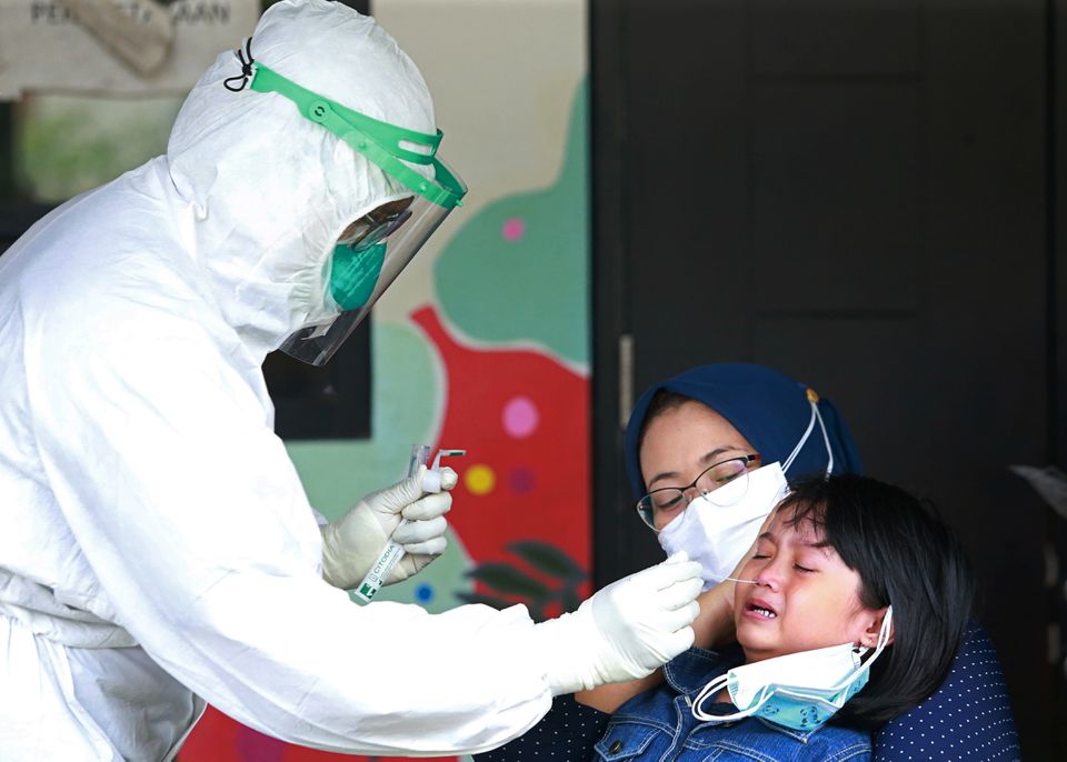 Một nhân viên y tế trong trang bị bảo hộ cá nhân lấy mẫu xét nghiệm COVID-19 từ một bé gái tại một trường học ở Jakarta, Indonesia