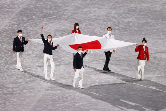 Các vận động viên Olympic Nhật Bản mang quốc kỳ của nước chủ nhà vào sân khi bắt đầu cuộc diễu hành của các nước trong lễ bế mạc