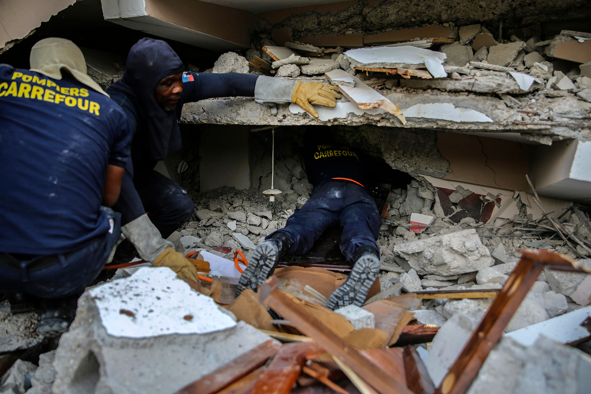 Lính cứu hỏa tìm kiếm những người sống sót giữa đống đổ nát ở Haiti.