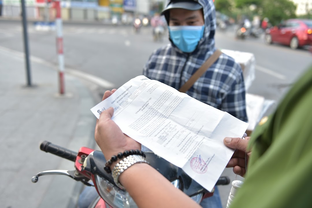 Nhân viên giao hàng xuất trình giấy đi đường để lực lượng chức năng kiểm tra khi thông hành.
