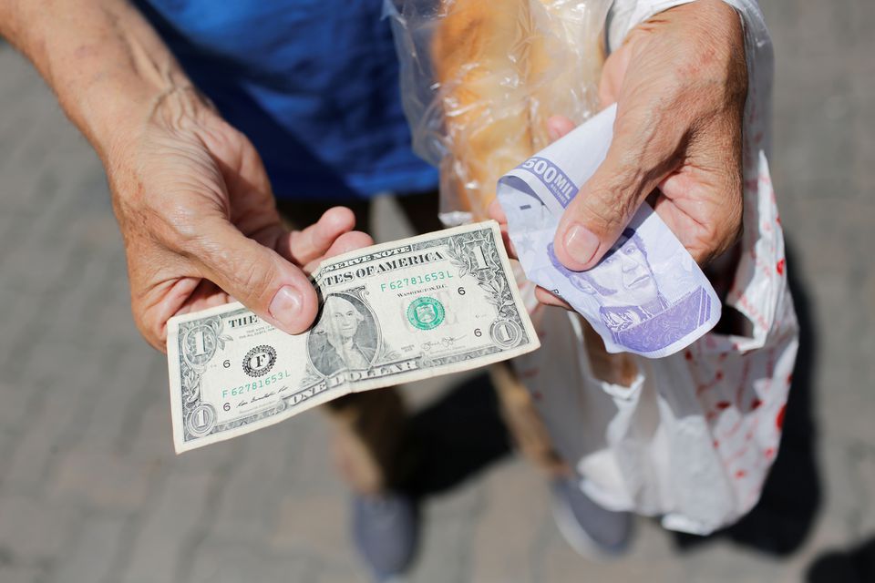 Một người bán hàng rong cầm tờ tiền 1 USD bên cạnh tờ tiền  500 triệu Bolivar cũ ở Caracas, Venezuela