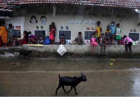 Học sinh chờ mưa tạnh để tiếp tục các lớp học ngoài trời ở Joba Attpara, Ấn Độ