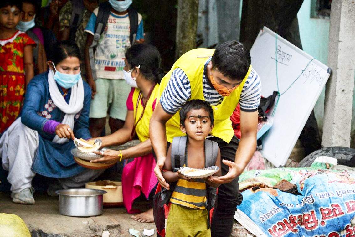 Tình nguyện viên tổ chức phi lợi nhuận Unique Foundation phân phát thực phẩm cho trẻ em ở khu dân cư có thu nhập thấp ngoại ô Siliguri, Ấn Độ - ẢNH: AFP