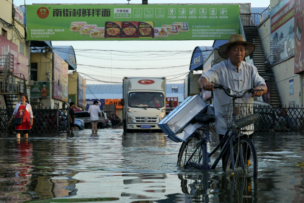 Một người đàn ông chở hàng trên xe đạp băng qua khu phố ngập nước ở Tân Hương, Hà Nam, miền trung Trung Quốc