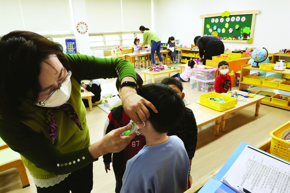 Một giáo viên kiểm tra thân nhiệt học sinh tại một trường mẫu giáo công lập ở Gwangju vào tháng 4/2021 - ẢNH:  YONHAP