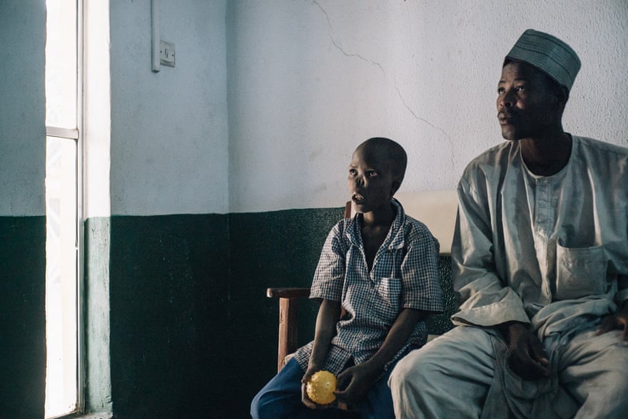 Adamu, một cậu bé 14 tuổi sống sót từ bang Kebbi đang đợi cha mình, Nadiri, để được các bác sĩ phẫu thuật kiểm tra. Ảnh: Claire Jeantet - Fabrice Caterini / Inediz