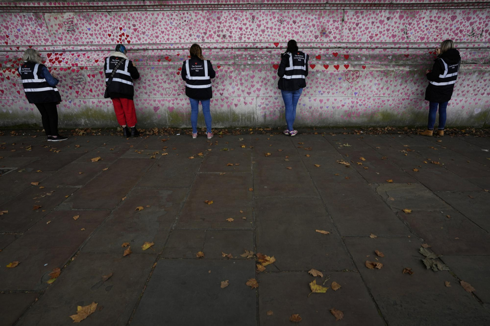 Các tình nguyện viên làm việc trên bức tường tưởng niệm COVID-19 ở Westminster, London. Mất khoảng 9 phút để một người đi bộ hết chiều dài của bức tường tưởng niệm mà không tạm dừng để đọc tên và chữ khắc