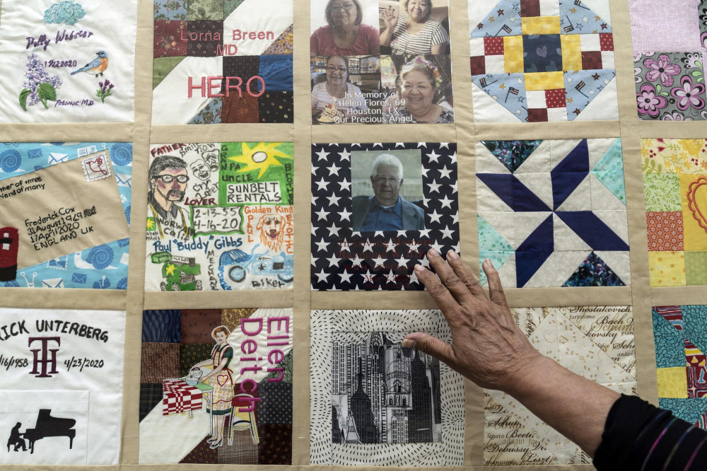 Một người đưa tay ra để chạm vào  những tấm vải COVID Memorial Quilt, một phần trong dự án của Madeleine Fugate nhằm tôn vinh và tưởng nhớ tất cả những người đã mất vì COVID-19, được trưng bày tại Trung tâm Khoa học California ở thành phố Los Angeles