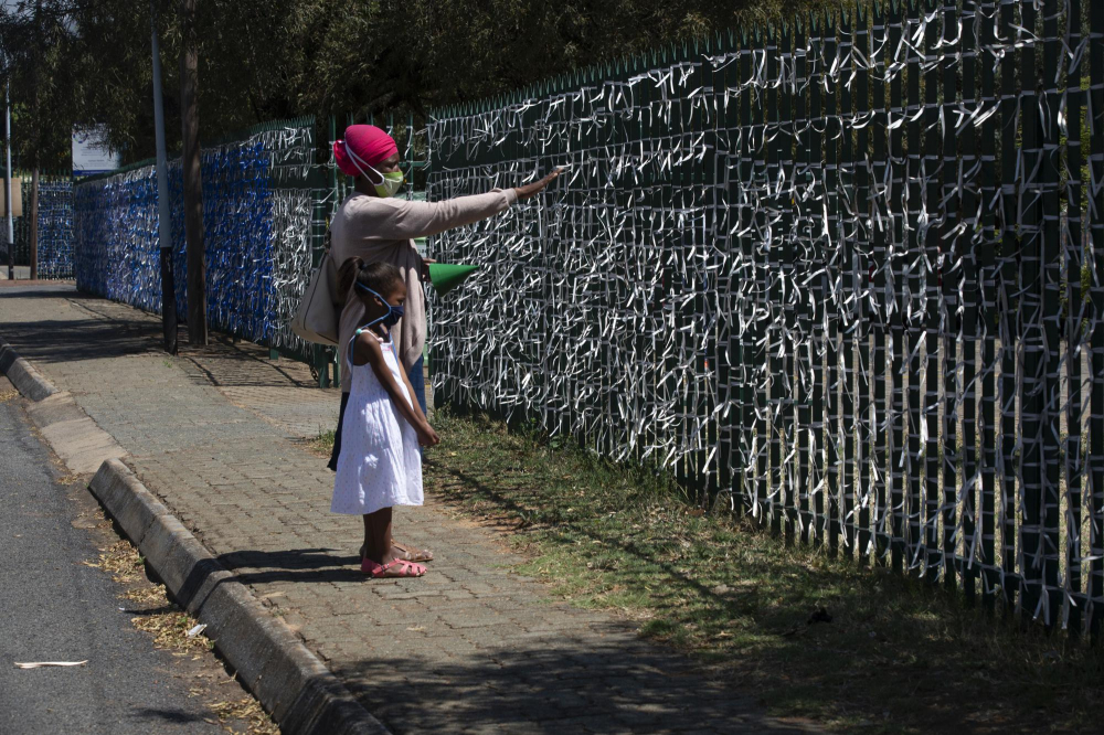 Một bà mẹ và đứa trẻ nhìn vào những dải ruy băng buộc vào hàng rào quanh Nhà thờ St. James Presbyterian ở Johannesburg. Chúng đại diện cho 89.000 người đã chết vì COVID-19 của đất nước: mỗi dải băng màu xanh lam tượng trưng cho 10 sinh mạng, còn màu trắng cho 1 sinh mạng