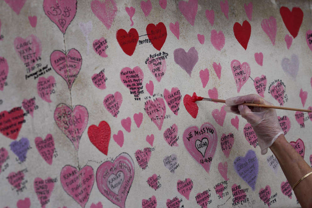 Một tình nguyện viên vẽ lại trái tim đã phai màu trên bức tường tưởng niệm nạn nhân COVID-19 ở Westminster, London, dọc theo bờ sông Thames. 
