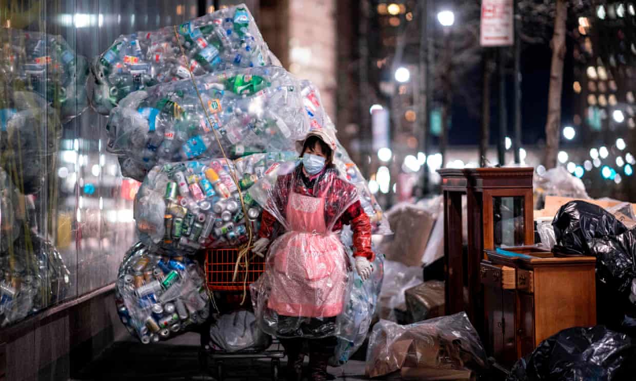 Một người phụ nữ đeo khẩu trang và đeo túi nhựa kéo một chiếc xe chở đầy túi rác tái chế qua các đường phố ở Lower Manhattan