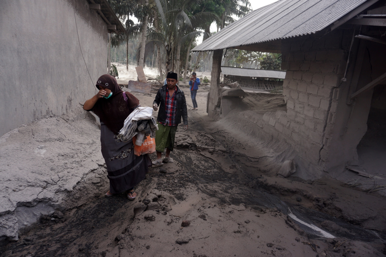 Dân làng mang đồ đạc của họ rời khỏi một ngôi nhà bị hư hại bao phủ bởi tro núi lửa tại làng Sumber Wuluh ở tỉnh Đông Java của Indonesia vào ngày 5 tháng 12 năm 2021. ẢNH: EPA-EFE