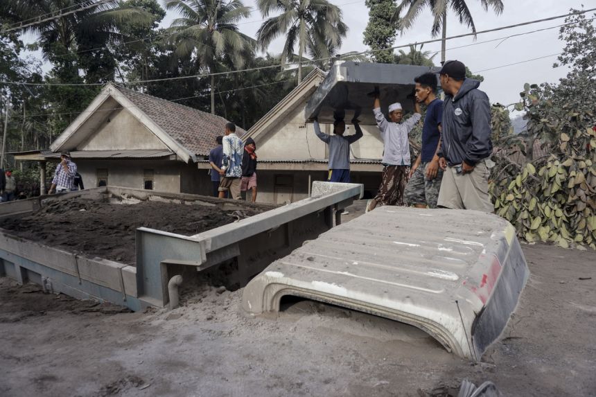 Dân làng mang đồ đạc của họ đến gần một chiếc xe tải bị chôn vùi dưới tro núi lửa từ vụ phun trào núi Semeru ở Đông Java vào ngày 5 tháng 12 năm 2021. ẢNH: EPA-EFE