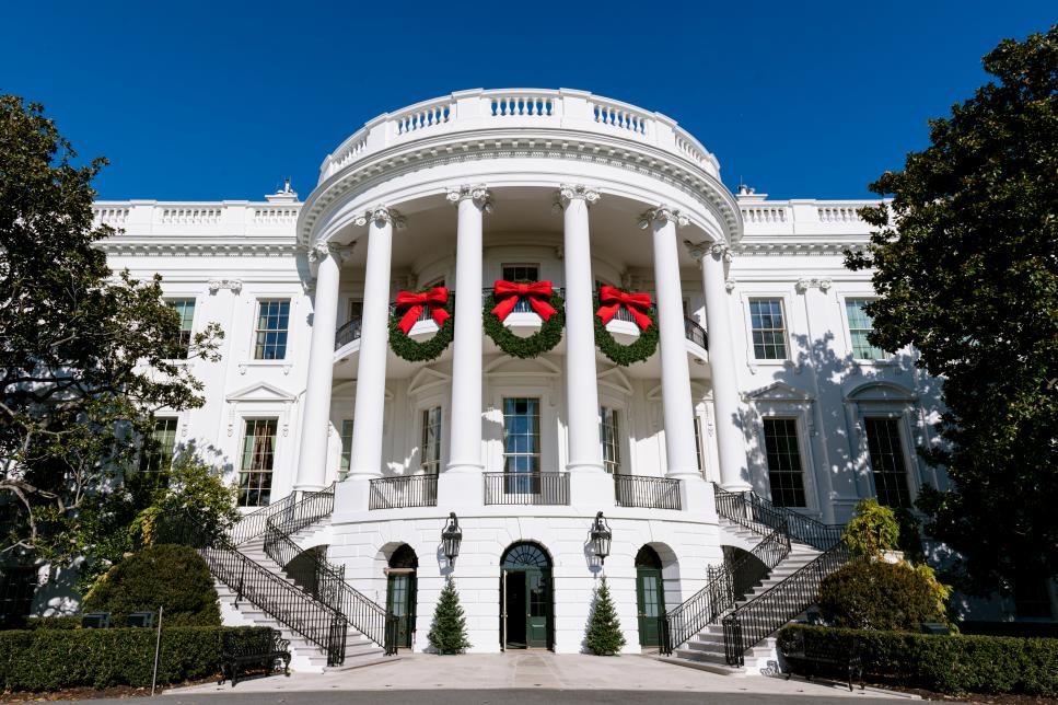 Bên ngoài của Nhà Trắng, nhìn từ Bãi cỏ phía Nam, được làm nổi bật bởi ba vòng hoa lớn với những chiếc nơ màu đỏ tươi.