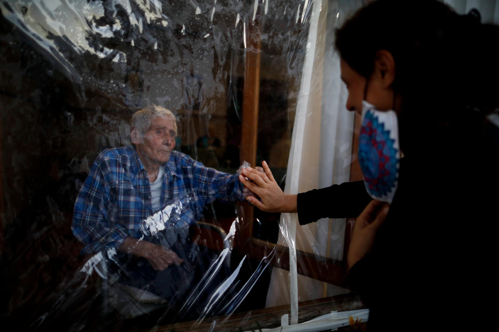 Victor Tripiana (86 tuổi) đưa tay ra để chạm vào bàn tay của con dâu Silvia Fernandez Sotto, được ngăn cách bởi một tấm nhựa theo quy định phòng COVID-19, tại dinh thự Reminiscencias dành cho người già ở Tandil, Argentina, ngày 4/4