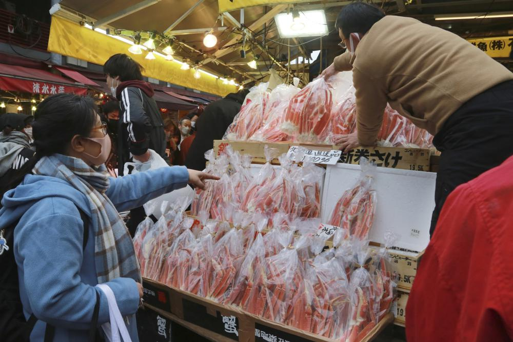 Người bán hải sản lấy hàng cho một người mua sắm cuối năm ở Tokyo vào thứ Sáu 31/12