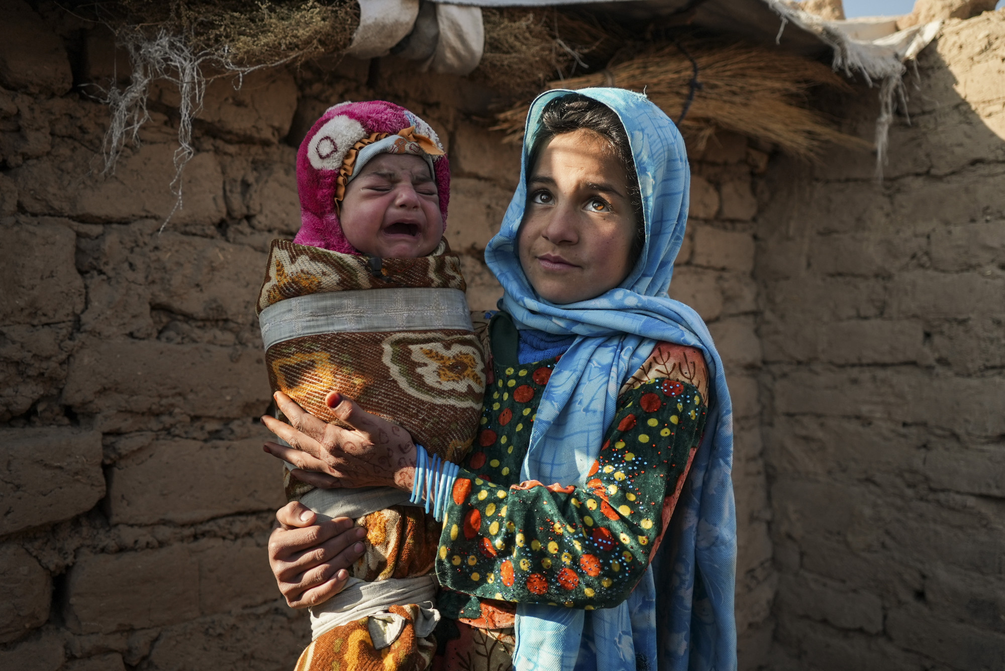 Qandi Gul ôm em trai bên ngoài ngôi nhà của họ ở Herat, Afghanistan, nơi họ tản cư để tránh chiến tranh và hạn hán 