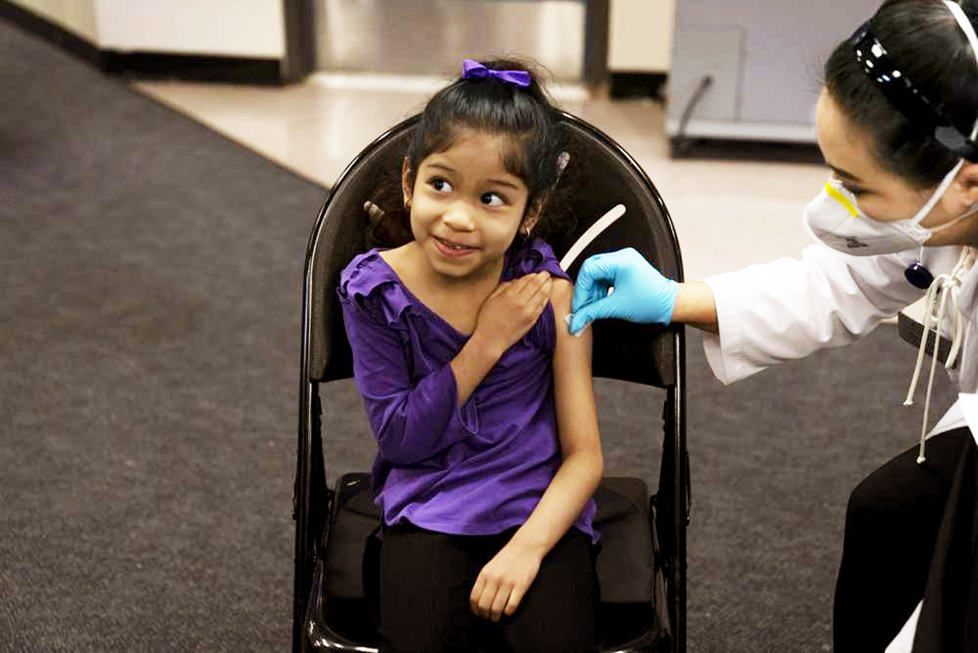 Elsa Estrada (sáu tuổi) ở bang California mỉm cười với mẹ khi được bác sĩ sát trùng da để tiêm vắc-xin COVID-19 - ẢNH: AP